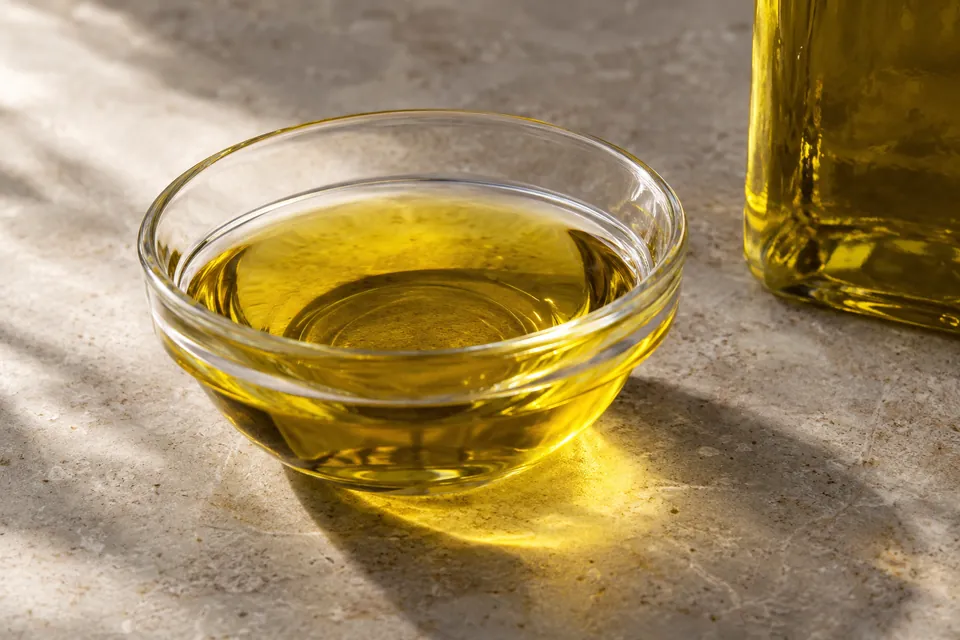 Golden oil in a glass bowl beside a partly cropped, unlabelled bottle.