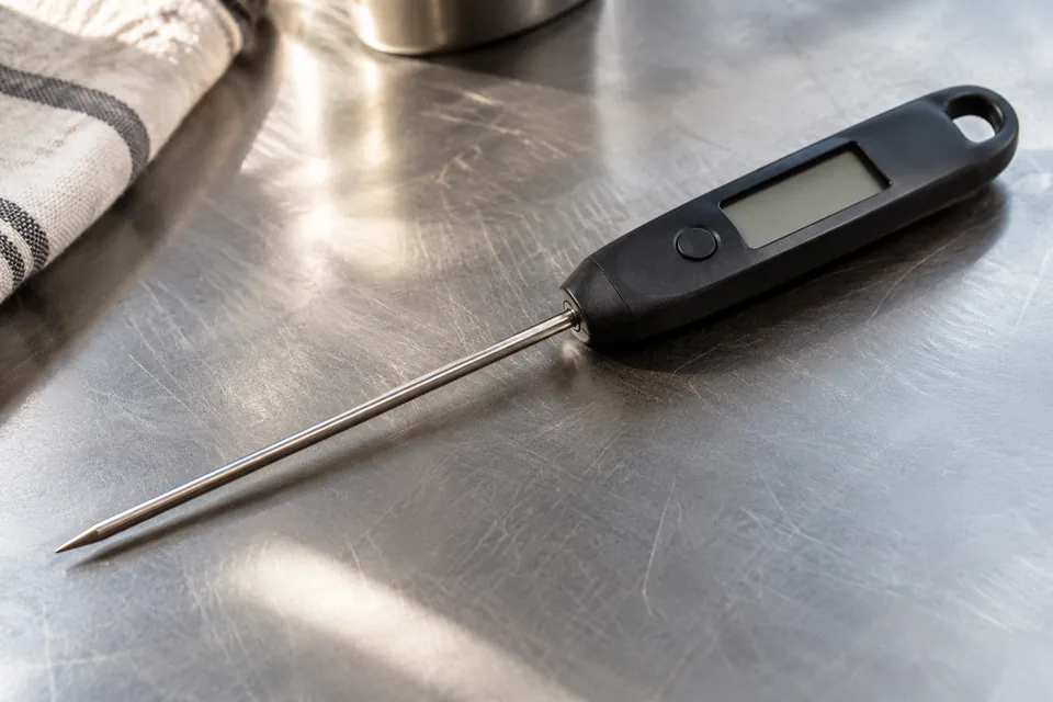A black probe thermometer lies diagonally on a metal counter, with its display unlit.