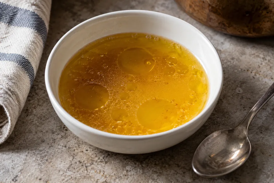 Rounded golden oil pools on the surface of sauce in a white bowl.